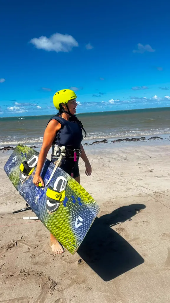 Aluna na areia com capacete e prancha de kitesurf