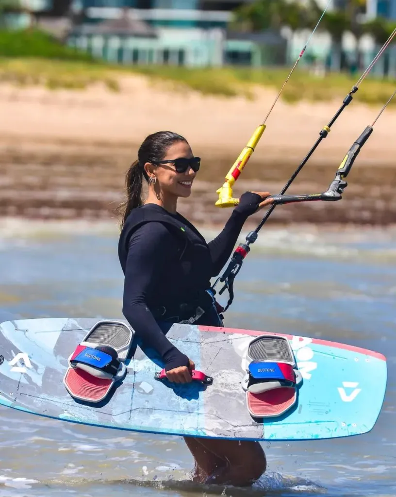 Aluna na água com prancha e barra de kitesurf