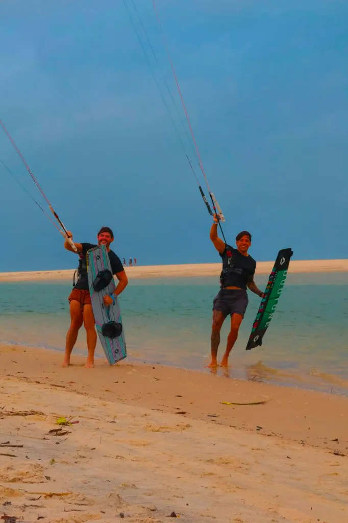 Dois alunos na praia com pranchas e barras de kite